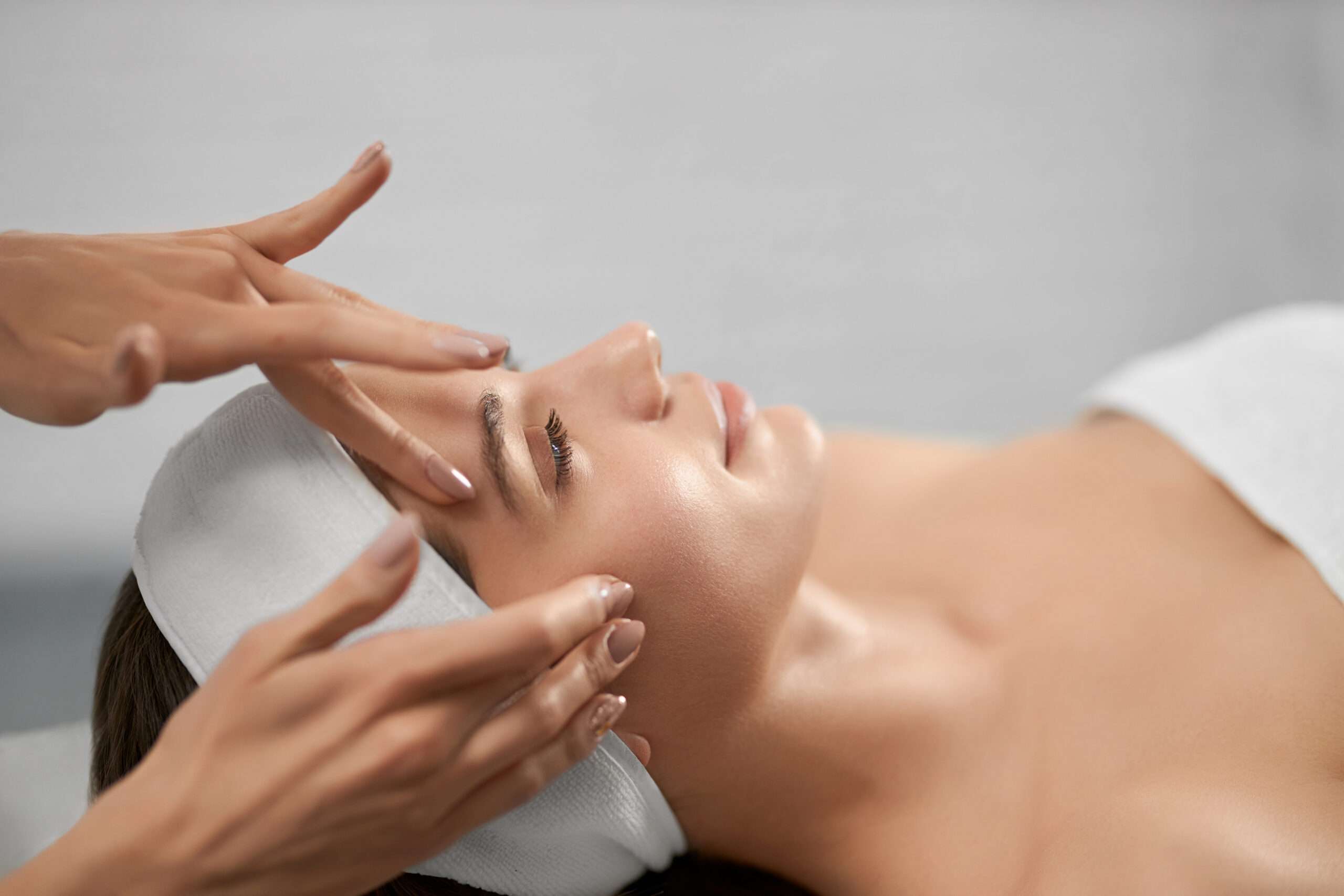 Side view of smiling young woman on procedure for improvements face skin in beautician. Concept of procedure for rejuvenation skin or improvements in professional salon.